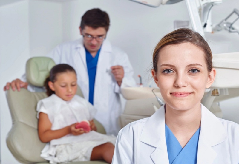 A child is sitting on a dental chair along with dental professionals in Parker, CO